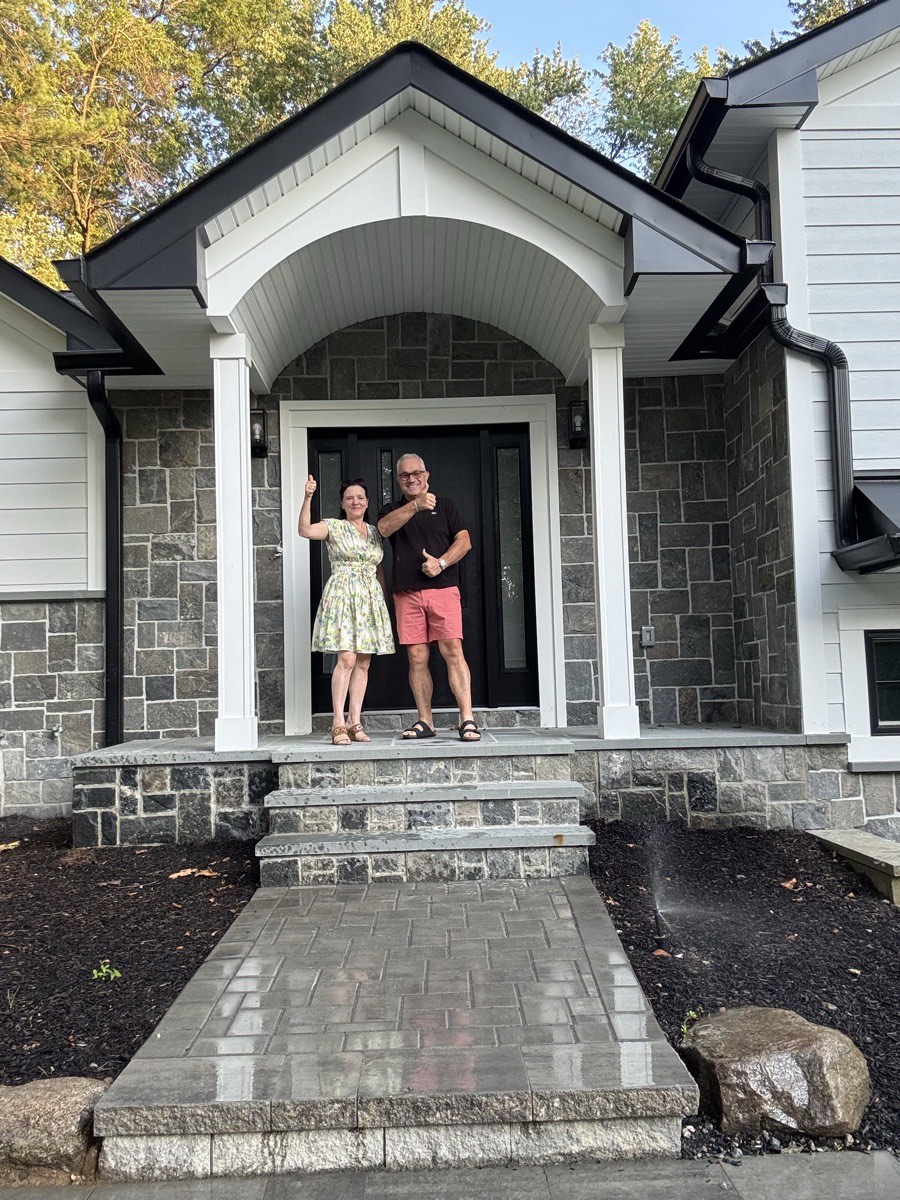 Dragan and Kosa Dinic giving a thumbs up at the arched stone entry of a newly completed custom home in Hillsdale, NJ built by Dadak LLC
